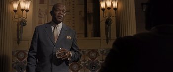 Movie still from “The Banker” (2020), directed by George Nolfi – An older man in a suit and tie holding a glass; Medium shot, Low angle