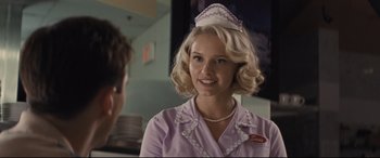 Movie still from “The Banker” (2020), directed by George Nolfi – A woman wearing a nurse's uniform and smiling for the camera; Close Up shot, Over the shoulder angle