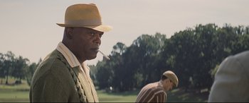 Movie still from “The Banker” (2020), directed by George Nolfi – A man with a hat smoking a cigarette in front of another man in a field; Medium shot, Over the shoulder angle