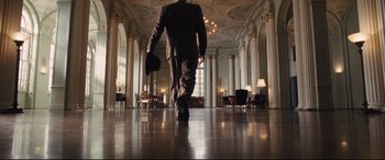 Movie still from “The Banker” (2020), directed by George Nolfi – A man in a suit walking through a lobby; Wide shot, Low angle