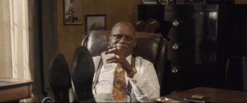 Movie still from “The Banker” (2020), directed by George Nolfi – A man sitting in a chair holding a glass of wine; Medium shot, Low angle