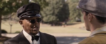 Movie still from “The Banker” (2020), directed by George Nolfi – An older man wearing a hat and sunglasses; Close Up shot, Over the shoulder angle