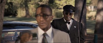 Movie still from “The Banker” (2020), directed by George Nolfi – A man in a suit and tie smoking a cigarette; Medium shot, Over the shoulder angle