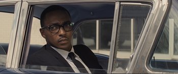 Movie still from “The Banker” (2020), directed by George Nolfi – A man sitting in the passenger seat of a car wearing a suit; Close Up shot, Over the shoulder angle