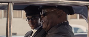 Movie still from “The Banker” (2020), directed by George Nolfi – A man in a suit and a man in a hat and glasses; Close Up shot, Over the shoulder angle