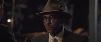 Movie still from “The Banker” (2020), directed by George Nolfi – A man in a suit and a hat and glasses; Close Up shot, Over the shoulder angle