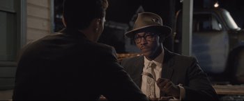 Movie still from “The Banker” (2020), directed by George Nolfi – A man in a suit and a hat talking to another man in a suit; Medium shot, Over the shoulder angle