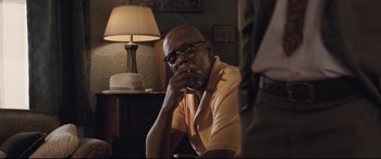 Movie still from “The Banker” (2020), directed by George Nolfi – A man sitting at a table with a cigarette in his mouth; Medium shot, Over the shoulder angle