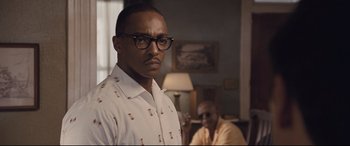 Movie still from “The Banker” (2020), directed by George Nolfi – A man with glasses standing next to another man in a living room; Close Up shot, Over the shoulder angle