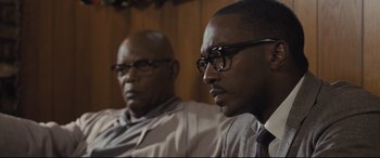 Movie still from “The Banker” (2020), directed by George Nolfi – Two men sitting next to each other in front of a wooden wall; Close Up shot, Over the shoulder angle