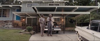 Movie still from “The Banker” (2020), directed by George Nolfi – A couple of men standing next to each other in front of a car; Wide shot, Low angle