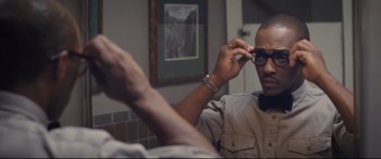 Movie still from “The Banker” (2020), directed by George Nolfi – A man holding a pair of eyeglasses while sitting down; Close Up shot, Over the shoulder angle