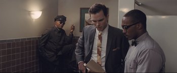 Movie still from “The Banker” (2020), directed by George Nolfi – A group of men standing next to each other in a room; Medium shot, Over the shoulder angle
