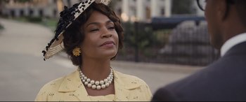 Movie still from “The Banker” (2020), directed by George Nolfi – An older woman wearing a yellow dress and a hat; Close Up shot, Over the shoulder angle