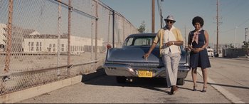 Movie still from “The Banker” (2020), directed by George Nolfi – A man standing next to an old car on the side of the road; Wide shot, Low angle