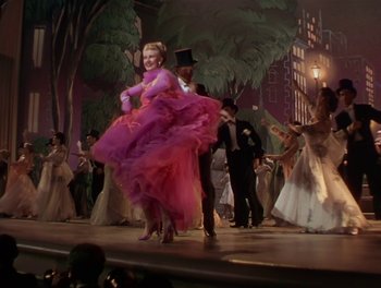 Movie still from “The Barkleys of Broadway” (1949), directed by Charles Walters – A woman in a pink dress and top hat on a stage; Wide shot, Low angle
