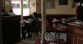Movie still from “The Beat That My Heart Skipped” (2005), directed by Jacques Audiard – A person sitting at a table with a lot of wine glasses; Wide shot, High angle