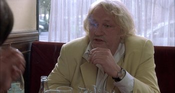 Movie still from “The Beat That My Heart Skipped” (2005), directed by Jacques Audiard – An older man sitting at a table smoking a cigarette; Close Up shot, Over the shoulder angle