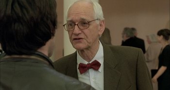 Movie still from “The Beat That My Heart Skipped” (2005), directed by Jacques Audiard – An older man wearing glasses and a red bow tie; Close Up shot, Over the shoulder angle