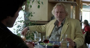 Movie still from “The Beat That My Heart Skipped” (2005), directed by Jacques Audiard – A man sitting at a table with a plate of food in front of him; Medium shot, Over the shoulder angle