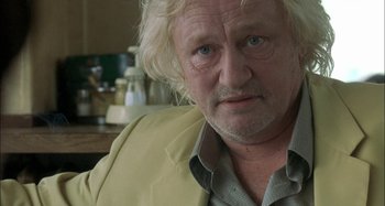 Movie still from “The Beat That My Heart Skipped” (2005), directed by Jacques Audiard – An older man with blonde hair and a beard; Close Up shot, Over the shoulder angle
