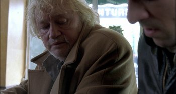 Movie still from “The Beat That My Heart Skipped” (2005), directed by Jacques Audiard – An older man with long blonde hair and a beard; Close Up shot, Over the shoulder angle