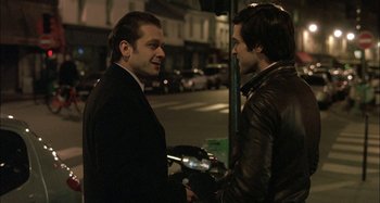 Movie still from “The Beat That My Heart Skipped” (2005), directed by Jacques Audiard – A couple of men standing next to each other on a street; Medium shot, Over the shoulder angle