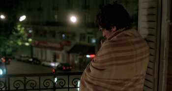 Movie still from “The Beat That My Heart Skipped” (2005), directed by Jacques Audiard – A man wrapped in a blanket looking out a window at night; Medium shot, High angle