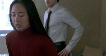 Movie still from “The Beat That My Heart Skipped” (2005), directed by Jacques Audiard – A man in a tie standing next to a woman in a red shirt; Medium shot, Over the shoulder angle