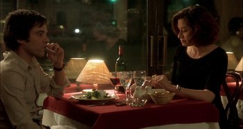 Movie still from “The Beat That My Heart Skipped” (2005), directed by Jacques Audiard – Two people sitting at a table with a plate of food and wine; Medium shot, Over the shoulder angle
