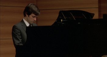 Movie still from “The Beat That My Heart Skipped” (2005), directed by Jacques Audiard – A man sitting at a grand piano in a room; Close Up shot, High angle