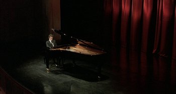 Movie still from “The Beat That My Heart Skipped” (2005), directed by Jacques Audiard – A man sitting at a piano in front of a red curtain; Extreme Wide shot, High angle