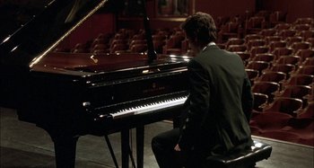 Movie still from “The Beat That My Heart Skipped” (2005), directed by Jacques Audiard – A man sitting at a piano in front of an audience; Medium shot, High angle