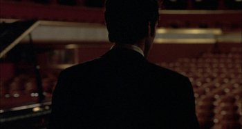 Movie still from “The Beat That My Heart Skipped” (2005), directed by Jacques Audiard – A man wearing a suit and tie standing in front of a building; Medium shot, Over the shoulder angle
