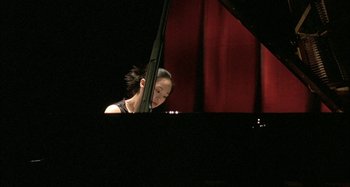 Movie still from “The Beat That My Heart Skipped” (2005), directed by Jacques Audiard – A woman sitting at a grand piano in front of a red curtain; Medium shot, High angle