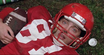 Movie still from “The Blob” (1988), directed by Chuck Russell – A football player laying on the ground wearing a helmet; Close Up shot, Overhead angle