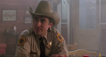 Movie still from “The Blob” (1988), directed by Chuck Russell – A man in a sheriff's uniform sitting in front of a table; Close Up shot, Low angle