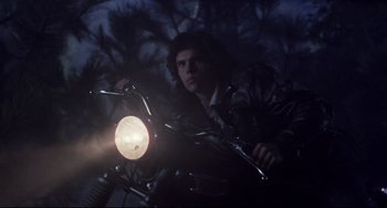 Movie still from “The Blob” (1988), directed by Chuck Russell – A man riding a motorcycle at night with a light on; Medium shot, Low angle