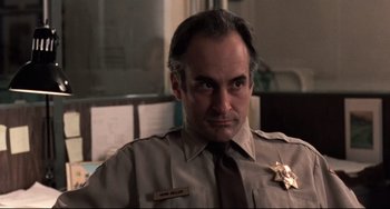 Movie still from “The Blob” (1988), directed by Chuck Russell – A man in a police uniform with a badge on his chest; Close Up shot, Low angle