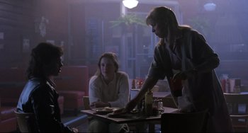 Movie still from “The Blob” (1988), directed by Chuck Russell – Two women and a man are sitting at a table; Medium shot, Over the shoulder angle
