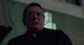 Movie still from “The Blob” (1988), directed by Chuck Russell – An older man wearing glasses and a priest's outfit; Close Up shot, Low angle