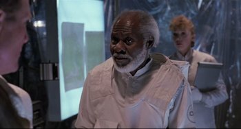 Movie still from “The Blob” (1988), directed by Chuck Russell – An older man in a white shirt is looking at a projector screen; Medium shot, Low angle