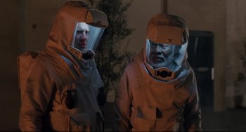 Movie still from “The Blob” (1988), directed by Chuck Russell – Two men in hazmat suits are standing in the dark; Medium shot, Over the shoulder angle