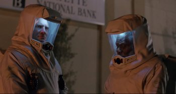 Movie still from “The Blob” (1988), directed by Chuck Russell – Two people in protective suits are standing in front of a building; Medium shot, Low angle