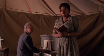 Movie still from “The Blob” (1988), directed by Chuck Russell – A woman standing next to an older man playing a piano; Medium shot, Low angle