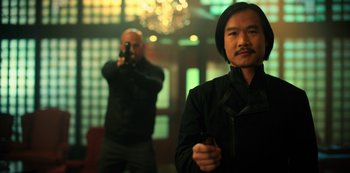 Movie still from “Altered Carbon” (2018), created by Laeta Kalogridis – A man holding a cell phone while standing next to another man; Medium shot, Low angle