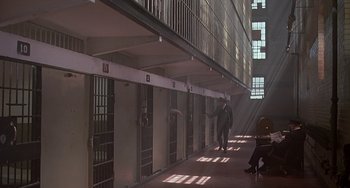 Movie still from “The Brink's Job” (1978), directed by William Friedkin – A person standing in a room next to a building; Wide shot, High angle