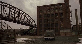 Movie still from “The Brink's Job” (1978), directed by William Friedkin – An old car parked in front of an old building; Extreme Wide shot, High angle
