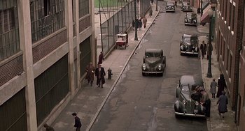 Movie still from “The Brink's Job” (1978), directed by William Friedkin – An old car is driving down the street with people; Extreme Wide shot, High angle