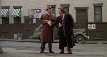 Movie still from “The Brink's Job” (1978), directed by William Friedkin – A couple of men standing next to each other on a street; Wide shot, Low angle
